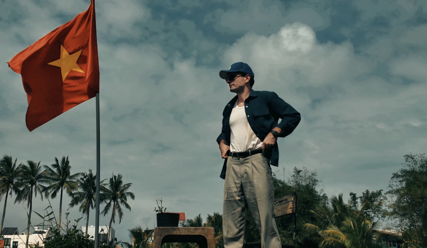 Matthew Barton standing beside a Vietnamese flag under palm trees